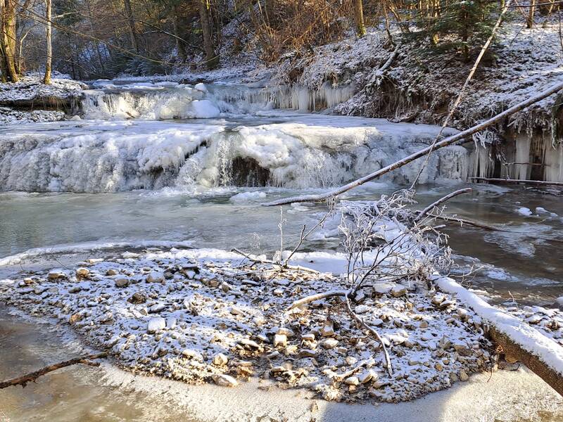 Ein zugefrorener Wasserfall und Bachlauf in einem winterlichen, schneebedeckten Wald.